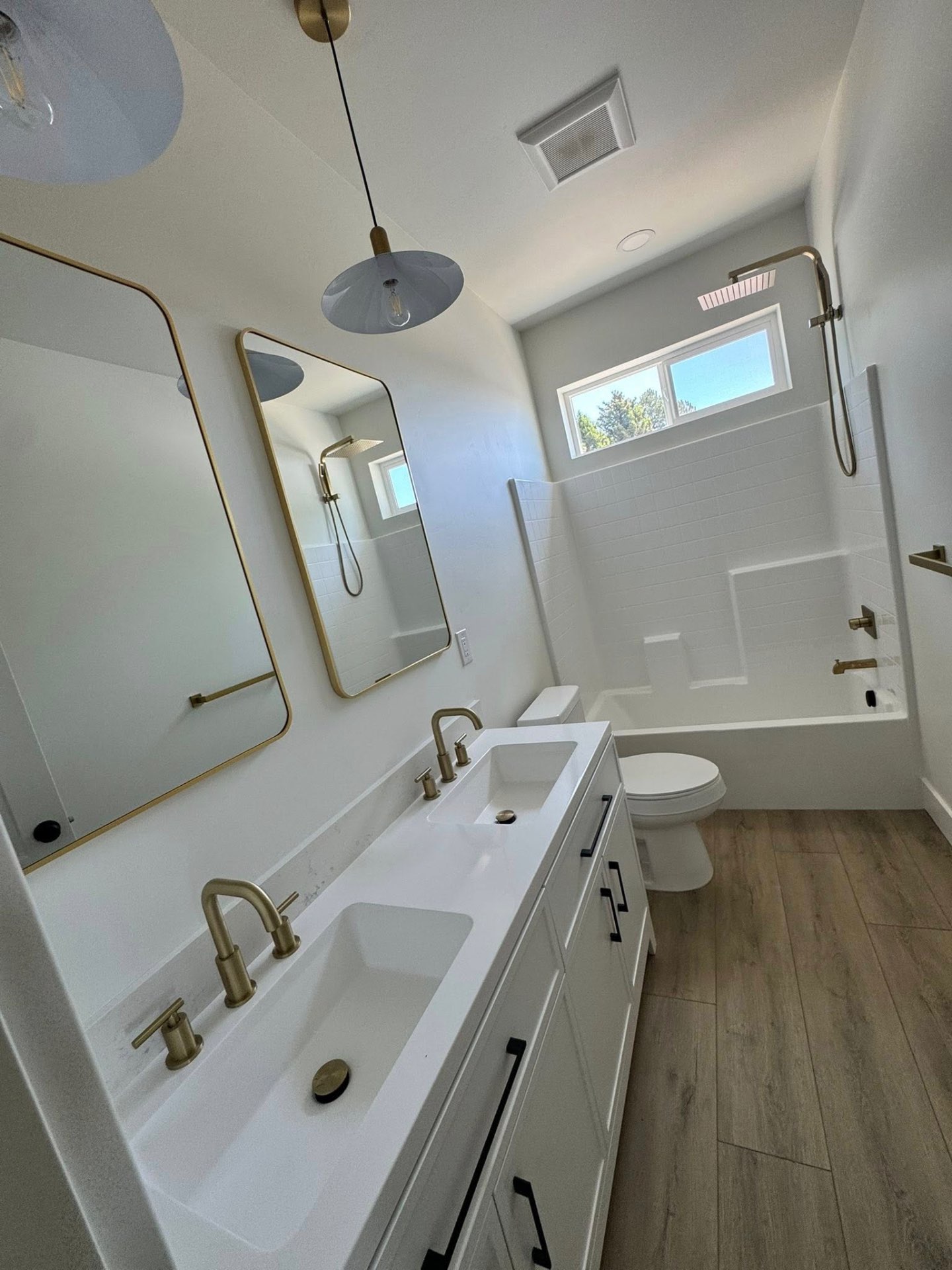 Bright bathroom remodel with double vanity, brass fixtures and tub surround